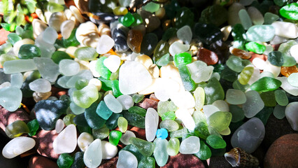 Stones and glass, sea pebbles of different colors in the shade with sunlight. natural background
