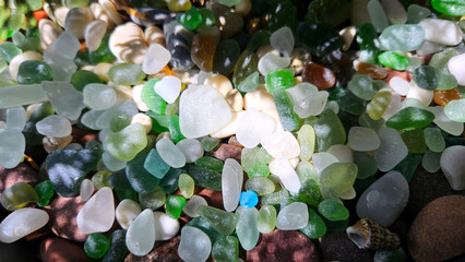 Stones and glass, sea pebbles of different colors in the shade with sunlight. natural background