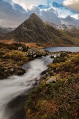 Tranquil mountain stream flows through a lush green meadow in Tryfan mountain, Wales