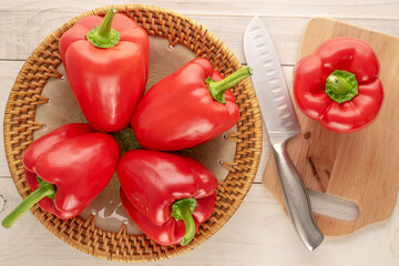 Several sweet red peppers with ceramic plate, knife and wooden kitchen board on wooden table, macro, top view.