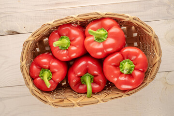 Several sweet red peppers in a basket on a wooden table, macro, top view.
