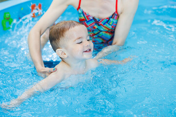 Fototapeta na wymiar A 2-year-old boy learns to swim in a pool with a coach. Swimming lessons for children. Swimming school for children. Educational swimming courses for children