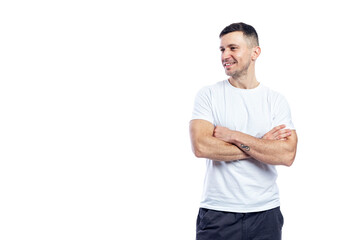 Fototapeta premium Laughing handsome man in a white t-shirt stands with crossed arms and looks away. Positive attitude and professionalism. Isolated on white background. Space for text.