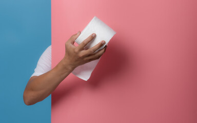 Male hand holding white toilet paper roll on blue background,copy space for text - obrazy, fototapety, plakaty