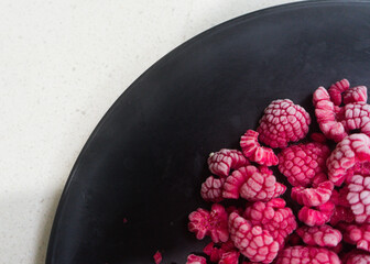 Flat lay of frozen raspberries on a black plate