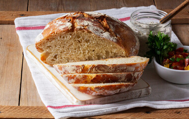 Round yeast bread made from white and whole grain flour, tomato salad and pate on a wooden background. Rustic style.