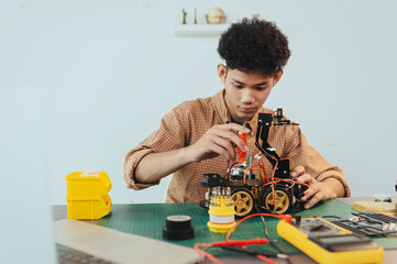 Fototapeta premium Asian young man assembling a robotic car, focus on robotics, assembling a robotic robot to develop intelligent robotics, mechanics students assembling a rescue robot car. Surveillance Robot.