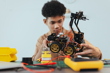 Asian young man assembling a robotic car, focus on robotics, assembling a robotic robot to develop intelligent robotics, mechanics students assembling a rescue robot car. Surveillance Robot.