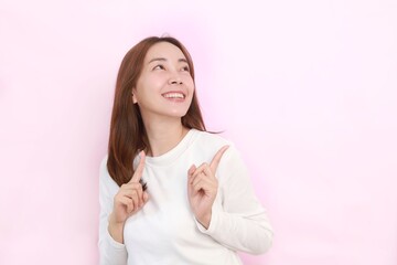 Smiling Asian woman standing over isolated pink background and pointing finger by the side to copy space.