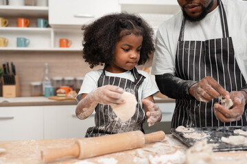 Happy African American kid girl and father cooking break or bakery with rolling bread in kitchen at...