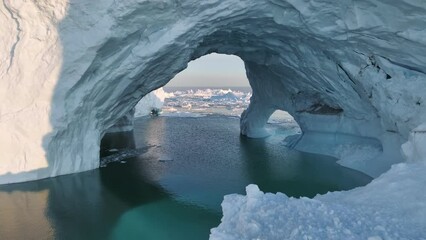Flying inside ice cave. Gaint iceberg with ice cave melting in the ocean. Icebergs from melting glacier float in Disco Bay, near Ilulissat, Greenland. Aerial shot, climate change concept