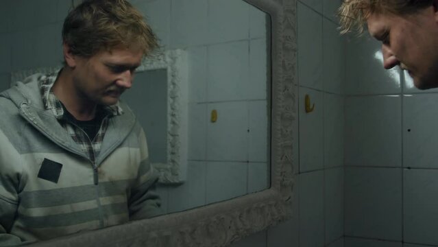 Tilt up shot of homeless man brushing his teeth in front of mirror in public toilet