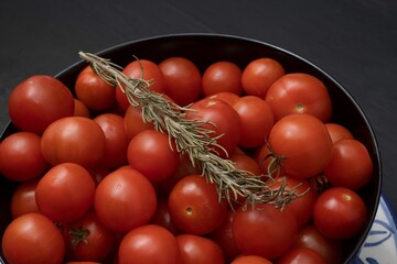 Close up shot of a bowl containing fresh, red tomatoes and a branch of fragrant rosemary