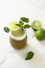 Vibrant cocktail in a small glass garnished with slices of lime and a sprig of mint