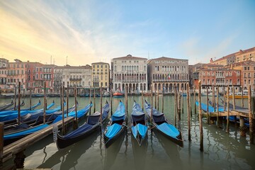 Naklejka premium Picturesque scene of gondolas on canal in Venice, Italy, surrounded by urban buildings at sunset