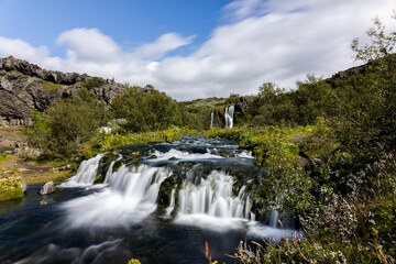 Scenic waterfall cascading down a rocky terrain, surrounded by lush green vegetation in Gjain valley