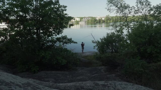 Person taking pictures of the lake on the shore covered with trees
