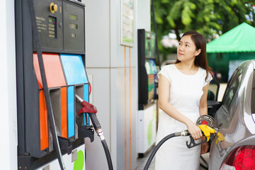 Happy Asian woman refueling a vehicle gas at gas station, self-service at gas station concept.