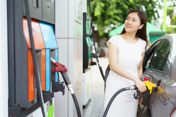 Happy Asian woman refueling a vehicle gas at gas station, self-service at gas station concept.