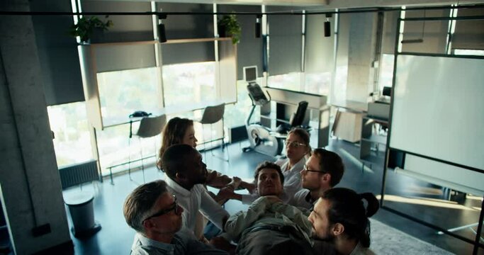 A brunette man in a blue shirt falls into the arms of his colleagues. Trust therapy. The blind fall