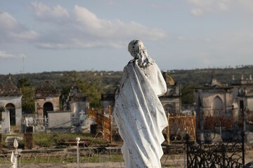 Beautiful statue standing on a hilltop cemetery, with historic buildings in the backdrop