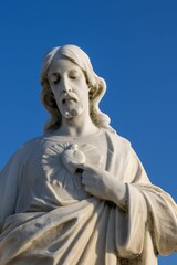 Fototapeta premium White statue of Jesus against a backdrop of a bright blue sky