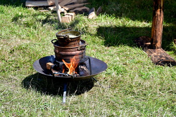 A close up on a wooden or clay pot standing on a fire pit used to melt some bee wax in order to make handmade candles and decorations seen during a medieval fair on a Polish countryside