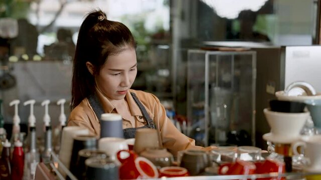 The beautiful Asian barista daughter prepares to make coffee for customers. coffee maker behind the bar counter in a cafe with intention Alone in the store. Owner of a small coffee shop business