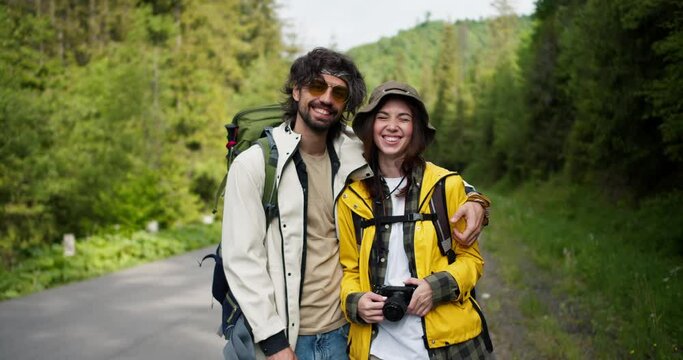 A guy and a girl tourists in special clothes for hiking pose with a camera against the backdrop of a mountain forest