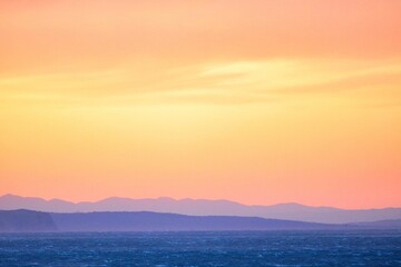 Obraz premium Scenic view of a stunning sunset over the ocean, with colorful mountains in the background