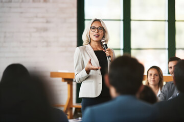 A confident female executive masterfully delivers a business presentation in a boardroom, engaging her audience during an informative workshop - obrazy, fototapety, plakaty
