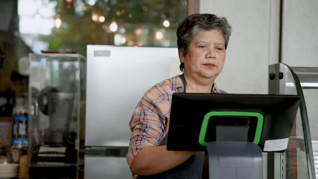 An elderly Asian barista runs a small business as a coffee shop. Taking orders from customers And record the information in the cash register behind the bar counter. and prepare to make coffee