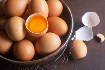 Chicken eggs in a bowl with a cracked egg showing fresh yolk