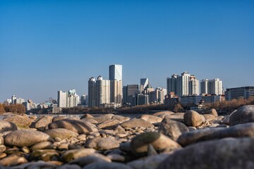 Pebbles on a rocky shoreline, featuring a view of distant buildings in the background