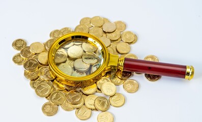 Golden coin lies amongst a heap of coins, illuminated by a magnifying glass