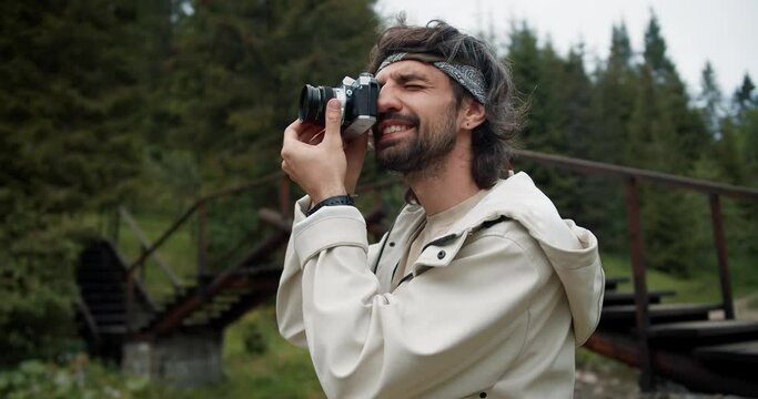 Portrait of a tourist brunette guy who photographs a view of the green forest. Guy in a white jacket on a hike