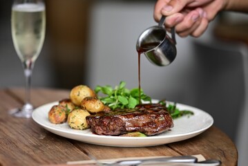 Person pouring sauce on meat with fried potatoes