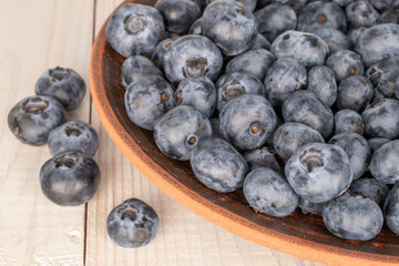 A few juicy blueberries in a clay plate on a wooden table, macro.