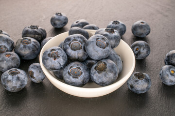 A few juicy blueberries in a white ceramic saucer on a slate stone. macro.