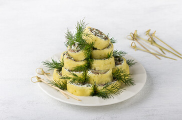 Delicious cheese roll stuffed with cream cheese, herbs and mushrooms on a white plate in the shape of a Christmas tree, decorated with greens on a light gray table