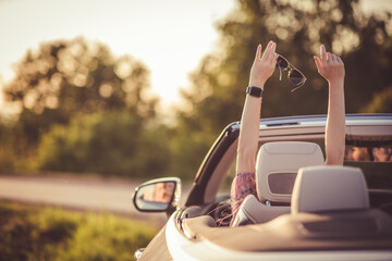 Happiness in a convertible. Young woman driving a car during sunset. - 630826961