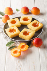 Square soft cookies with apricot jam close-up on a plate on the table. Vertical