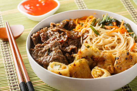 Vietnamese Beef Noodle Salad Bun Bo with crispy nem spring rolls and vegetables closeup on the table. Horizontal