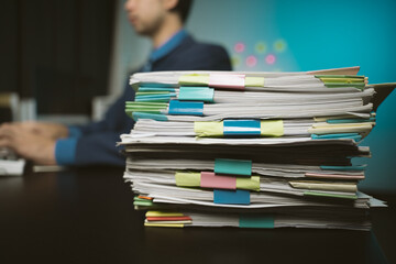 Businessman man working in stacks of papers searching for unfinished paperwork information on form check stack on table and checking financial papers in busy workload