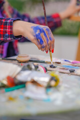 Close-up of a girl painter's hands in paint who takes oil paint from a palette with a brush in a studio for painting 