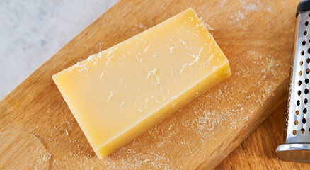 block of grated cheese on a wooden board and a grater