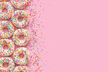 festive background of donuts with sprinkles and icing over pink background, copy space