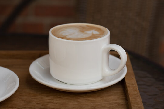 white ceramic cup of coffee with milk picture on wooden tray. Morning coffee