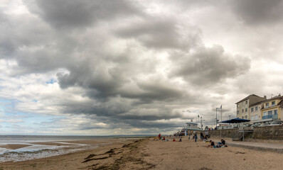 Fototapeta na wymiar Langrune-Sur-Mer, France - 07 19 2023: View of a cloudy rainy sky, the seawall, beach cabins and people above the sea from the beach.