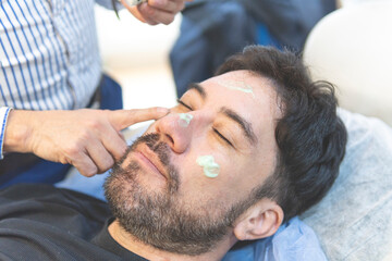 Obraz na płótnie Canvas Latino man getting cosmetic treatment on his face